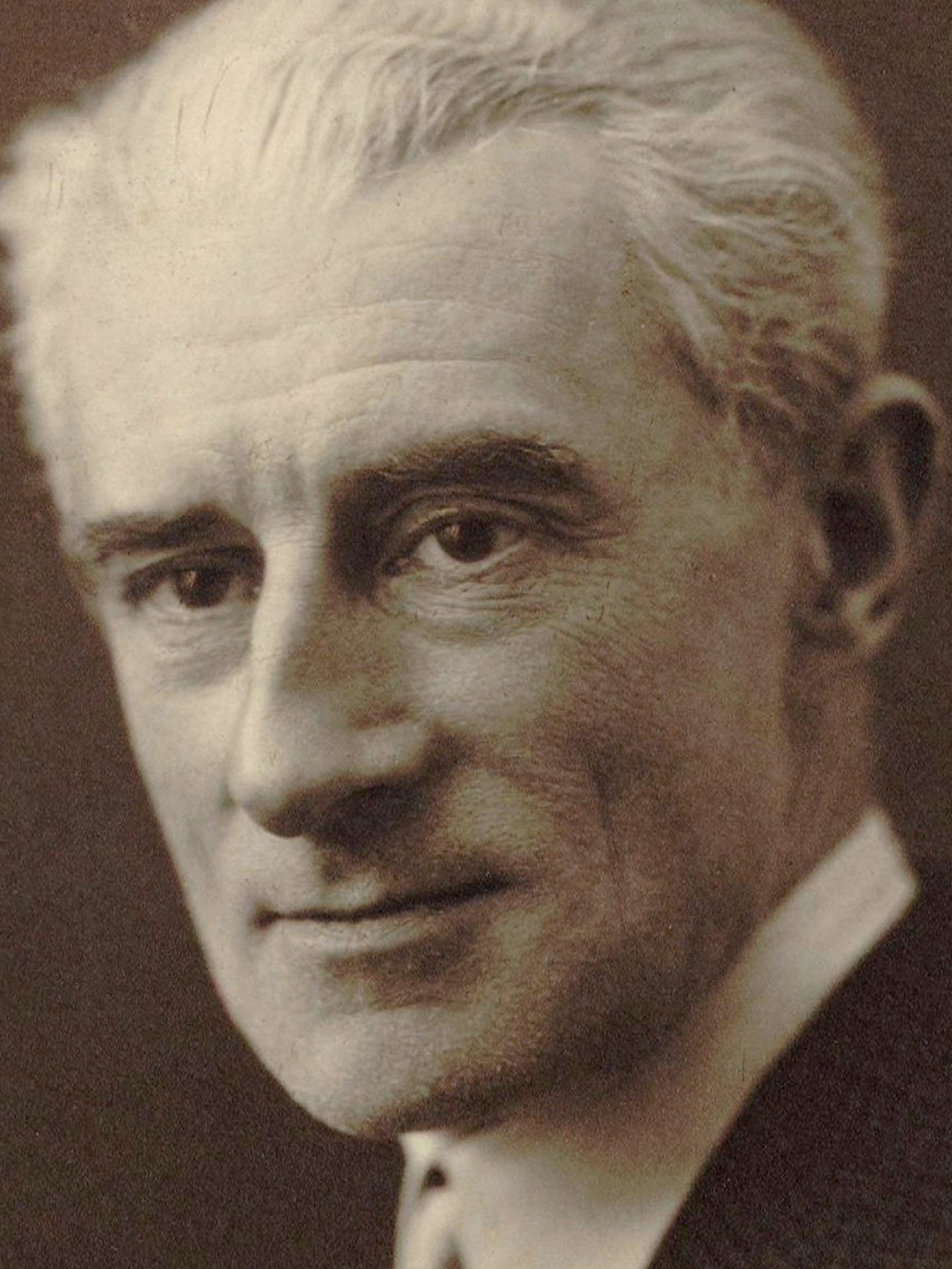 Portrait noir et blanc d'un homme âgé, en costume, avec les cheveux blancs et une expression souriante.