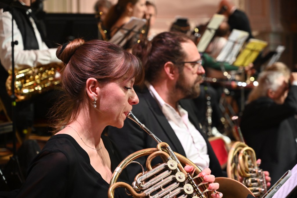 Musiciens jouant des instruments à vent lors d'un concert, avec un focus sur une femme jouant du cor.